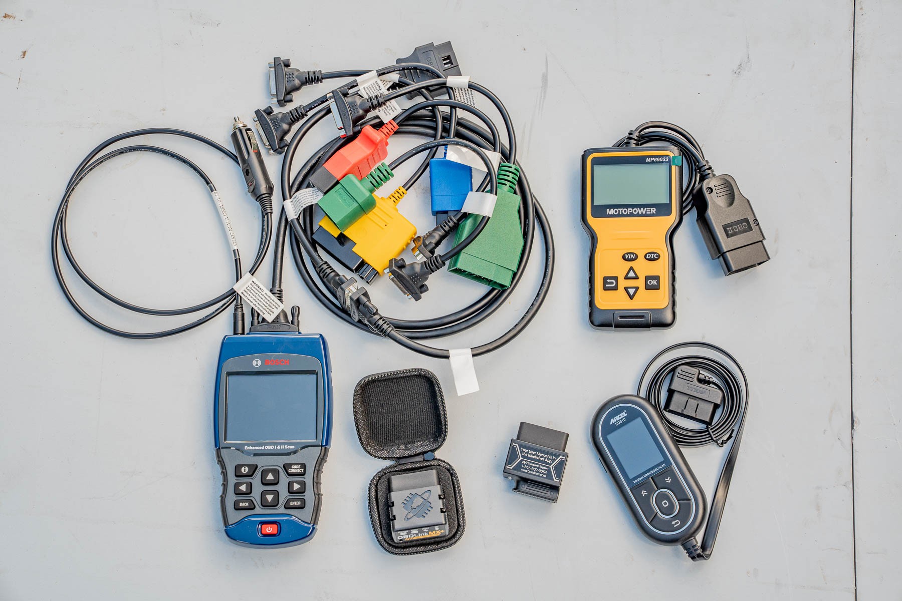 A variety of OBD2 scanners laid out on a surface, showcasing the different types and form factors available