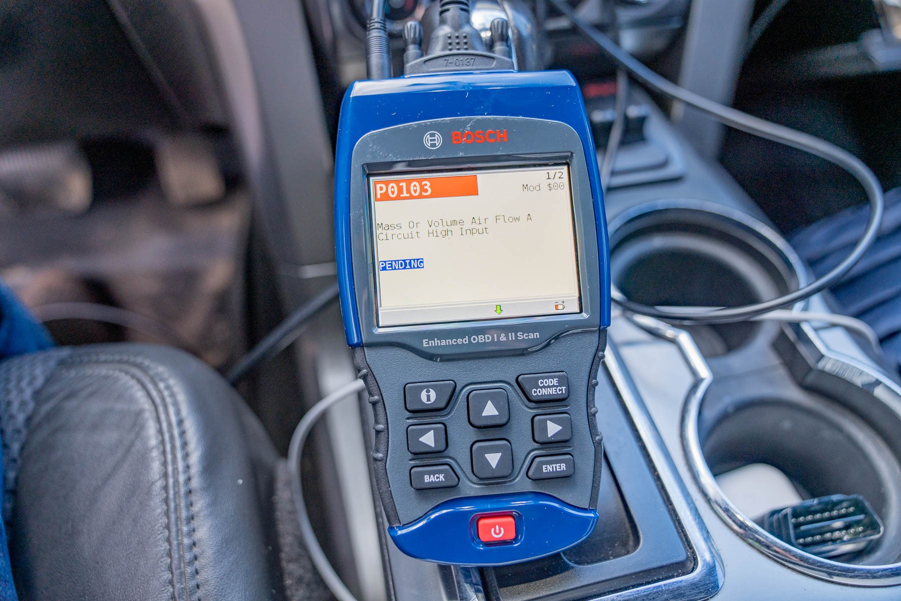 Bosch 1300 OBD scanner being used inside a car, plugged into the OBD2 port under the dashboard